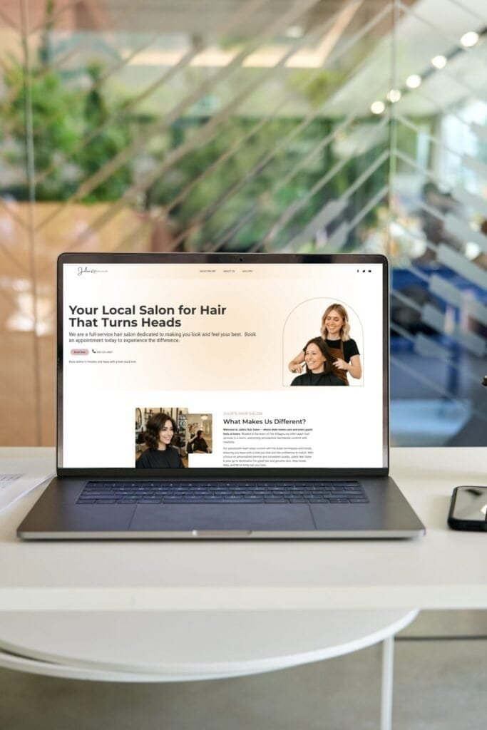 Laptop screen featuring Julie’s Hair Salon website in a stylish office setup with blurred glass background.