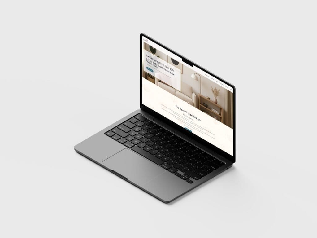Angled side view of a laptop on a light background displaying the redesigned Declutzy homepage with a minimalist living room image and calming neutral tones promoting decluttering services.